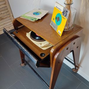"Régis" est un magnifique meuble "La voix de son maître" des années 50, à pieds compas sur roulettes et barres transversales en métal noir. Sa porte abattant ouvre sur une tablette coulissante recevant une platine "Elac Miraphon 120". Une ouverture à l'arrière du meuble a été créée pour accéder plus facilement aux câblages. "Régis" peut aisément être transformé en petit bureau d'appoint, l'abattant permettant d'y ranger un clavier et quelques papiers.  Laissé volontairement avec ses marques du temps pour lui donner plus d'authenticité. Disque 45 tours "microsillon"
