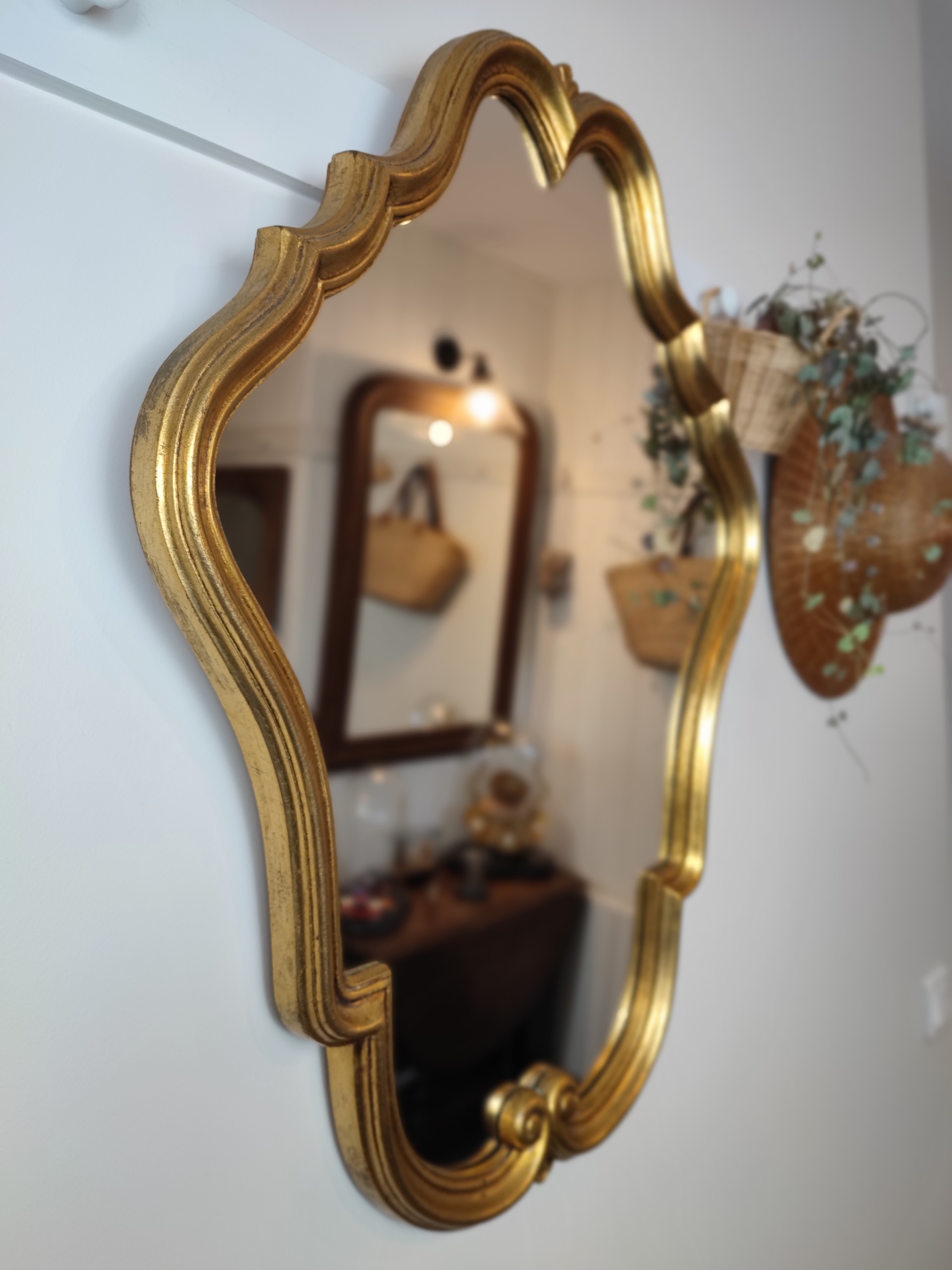 Grand miroir baroque "Angèle" mouluré finition doré. Un vrai miroir de conte de fée à installer dans une entrée. Elégant, chic et sobre à la fois. Chapeau de paille et plante verte dans un panier accroché à une patère murale.