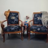 Ces deux fauteuils "Barthélemy & Bartholomée" de style Empire ont été partiellement rénovés en parfaite harmonie avec l’intérieur de la cliente. Le tissu d’origine, devenu démodé, a laissé place à un somptueux velours noir orné d’un motif de tigre doré, soigneusement choisi par la cliente elle-même. Ce choix audacieux et raffiné s’accorde idéalement avec son univers décoratif peuplé de figurines ramenées des quatre coins du monde. La rénovation a impliqué une dépose complète du dossier afin de garantir une finition soignée. Pour moderniser l’ensemble, une finition avec des clous décoratifs noir mat a été proposée et acceptée immédiatement, ajoutant ainsi une touche contemporaine et élégante.