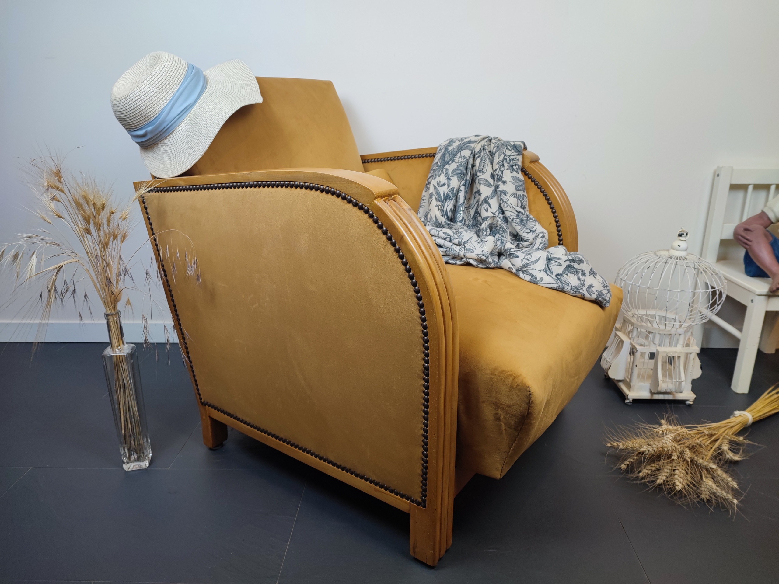 Entre lignes géométriques et chaleur du bois, André(e) incarne toute l’élégance du style Art déco. Entièrement rénové, ce fauteuil des années 1920 retrouve son éclat d’origine tout en adoptant une touche contemporaine. La structure en hêtre massif a été soigneusement poncée, traitée et éclaircie avant d’être protégée par un verni à la teinte chêne doré satiné, pour s'accorder au mieux aux fauteuils existants des clients. L’assise et le dossier ont été refaits selon les techniques traditionnelles et recouverts d’un velours miel profond, doux et lumineux, qui met en valeur la finesse des accoudoirs galbés et les détails d’époque. Chaque finition est le fruit d’un travail patient et exigeant : les coutures, invisibles, sont réalisées à la main, dans le respect du fauteuil et de son époque. Son dossier basculant offre un confort supplémentaire, parfait pour un moment de lecture ou de détente.