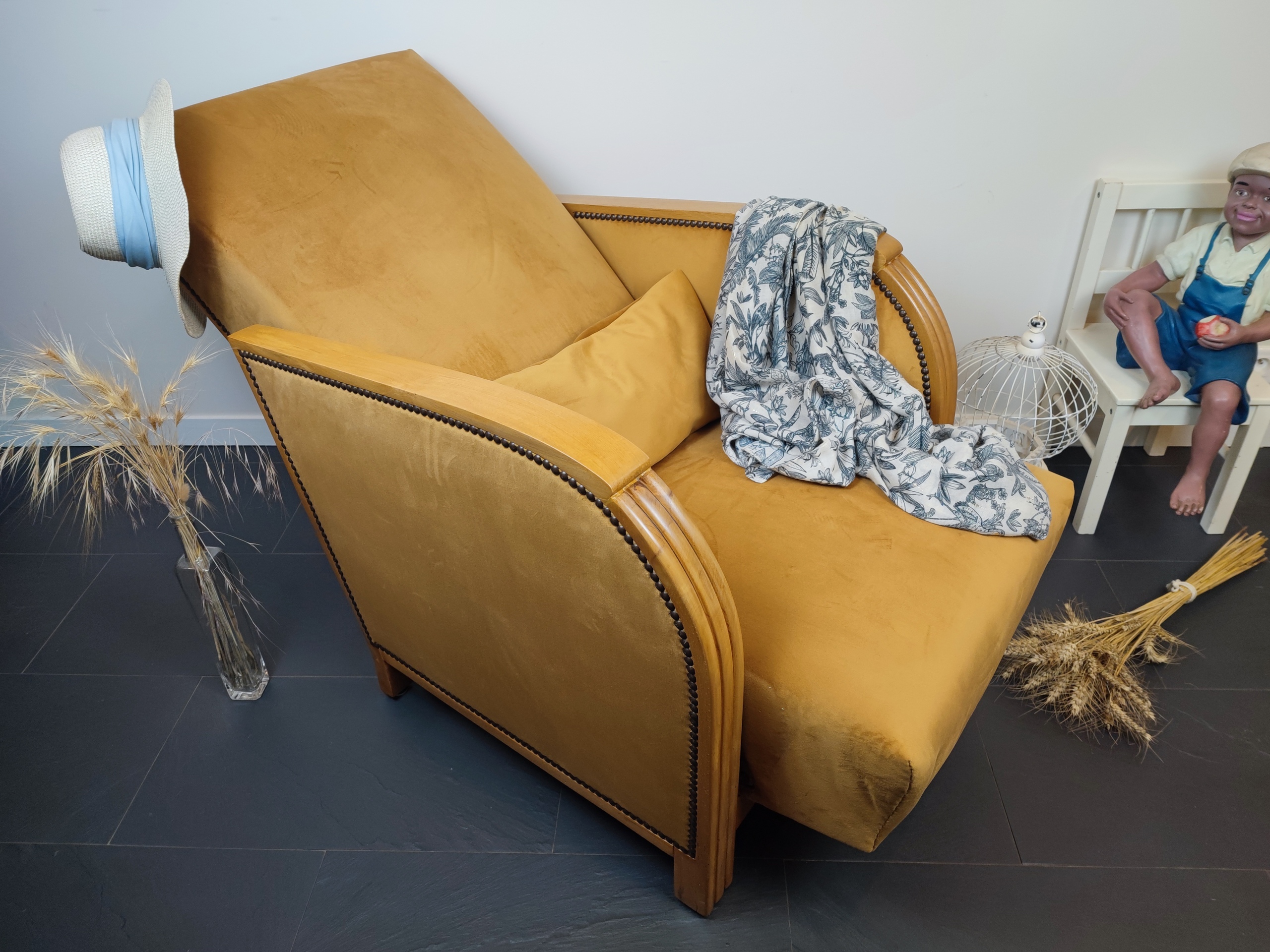 Entre lignes géométriques et chaleur du bois, André(e) incarne toute l’élégance du style Art déco. Entièrement rénové, ce fauteuil des années 1920 retrouve son éclat d’origine tout en adoptant une touche contemporaine. La structure en hêtre massif a été soigneusement poncée, traitée et éclaircie avant d’être protégée par un verni à la teinte chêne doré satiné, pour s'accorder au mieux aux fauteuils existants des clients. L’assise et le dossier ont été refaits selon les techniques traditionnelles et recouverts d’un velours miel profond, doux et lumineux, qui met en valeur la finesse des accoudoirs galbés et les détails d’époque. Chaque finition est le fruit d’un travail patient et exigeant : les coutures, invisibles, sont réalisées à la main, dans le respect du fauteuil et de son époque. Son dossier basculant offre un confort supplémentaire, parfait pour un moment de lecture ou de détente.