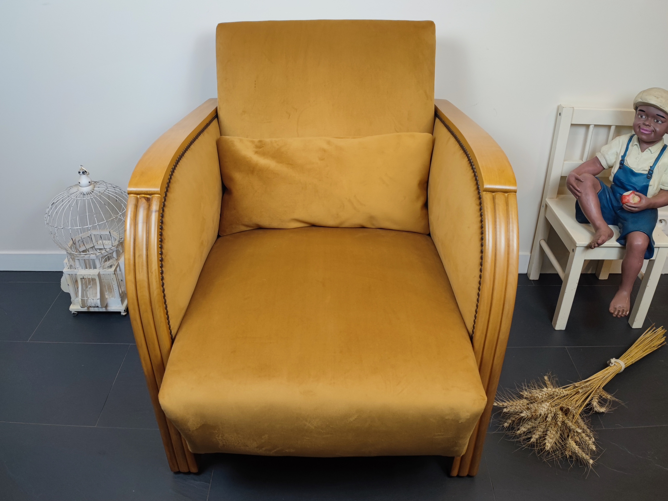 Entre lignes géométriques et chaleur du bois, André(e) incarne toute l’élégance du style Art déco. Entièrement rénové, ce fauteuil des années 1920 retrouve son éclat d’origine tout en adoptant une touche contemporaine. La structure en hêtre massif a été soigneusement poncée, traitée et éclaircie avant d’être protégée par un verni à la teinte chêne doré satiné, pour s'accorder au mieux aux fauteuils existants des clients. L’assise et le dossier ont été refaits selon les techniques traditionnelles et recouverts d’un velours miel profond, doux et lumineux, qui met en valeur la finesse des accoudoirs galbés et les détails d’époque. Chaque finition est le fruit d’un travail patient et exigeant : les coutures, invisibles, sont réalisées à la main, dans le respect du fauteuil et de son époque. Son dossier basculant offre un confort supplémentaire, parfait pour un moment de lecture ou de détente.